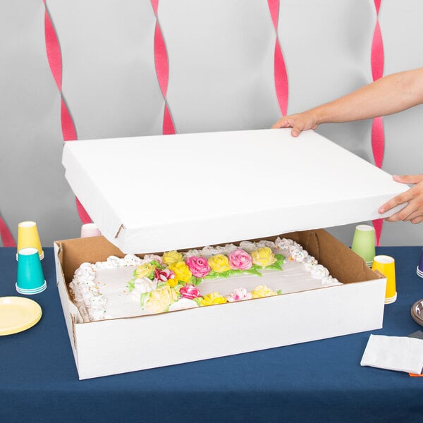 A person opening a 28" x 18" x 5" white bakery box with a cake inside.