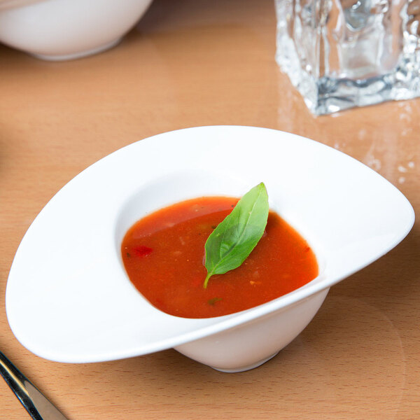 A white 10 Strawberry Street Somba porcelain bowl of soup with a basil leaf on top.