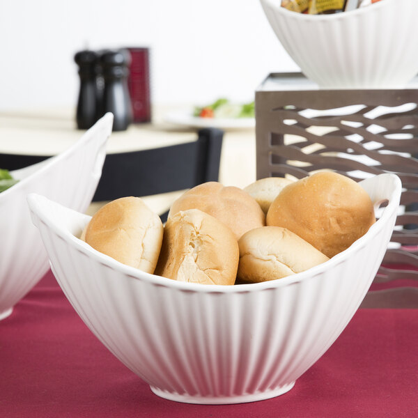 A white porcelain boat bowl with a line texture filled with bread rolls on a table.