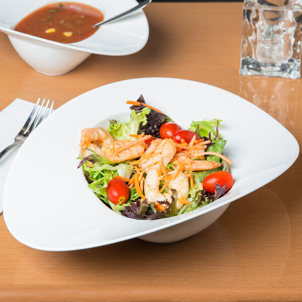 A bowl of salad with shrimp, tomatoes, and lettuce in a white oval bowl.