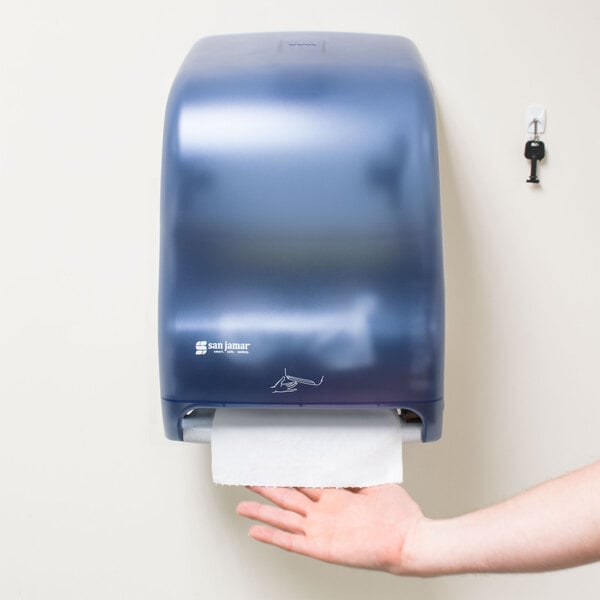 A hand using a San Jamar Arctic Blue paper towel dispenser.