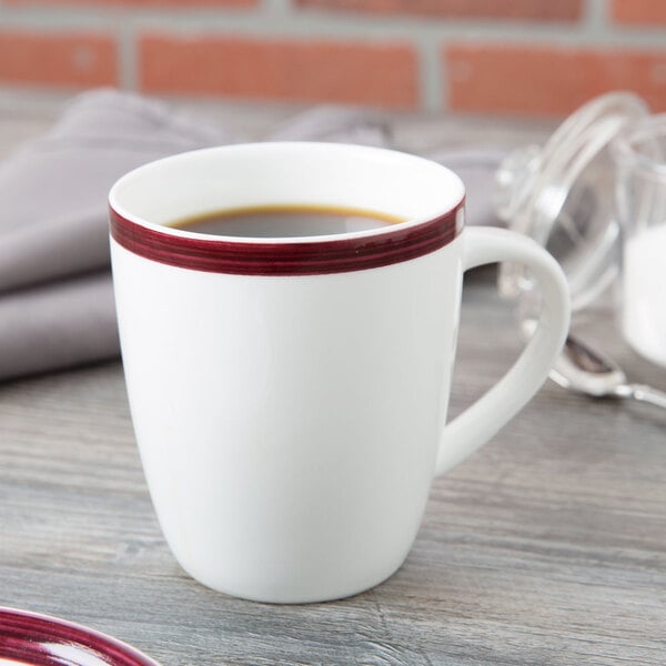 A white 10 Strawberry Street porcelain mug with a red stripe on the rim on a table with a cup of coffee.