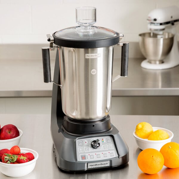 A Hamilton Beach food blender with a stainless steel container filled with fruit on a counter.
