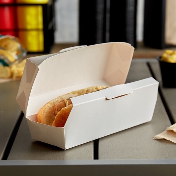 A hot dog in a 6 1/2" x 2 1/2" x 2 1/4" white paper container.
