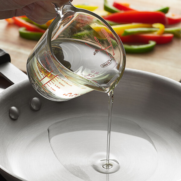 A hand pouring Admiration vegetable oil into a pan with vegetables.