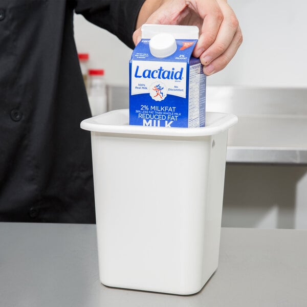 A person putting a carton of milk in a white Carlisle container.