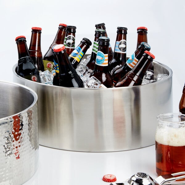 An American Metalcraft stainless steel double wall bowl filled with ice and beer bottles on a table.