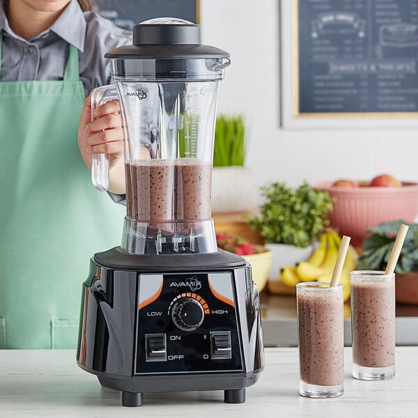A woman in an apron using an AvaMix commercial blender to make a smoothie.