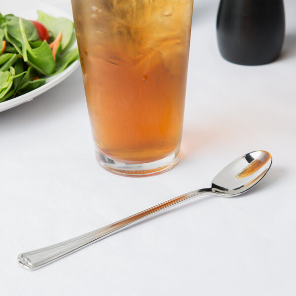 A Libbey stainless steel iced tea spoon in a glass of liquid on a table.