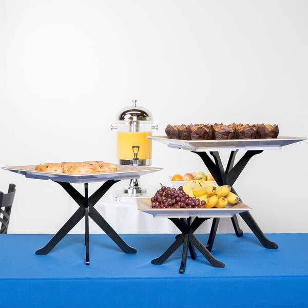 A Tablecraft black fold-a-way riser set with trays of food on a table.
