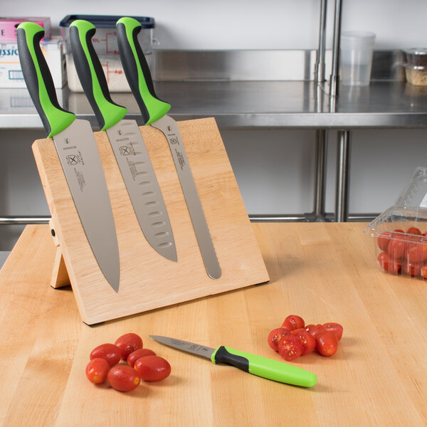 A Mercer Culinary Millennia Colors knife set with green handles on a wooden board with tomatoes.
