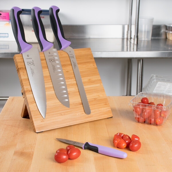 A Mercer Culinary Millennia Colors knife set with purple handles on a bamboo magnetic board.