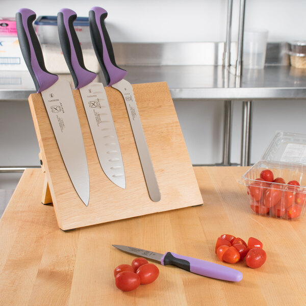 A Mercer Culinary Millennia knife set with purple handles on a wooden magnetic board.
