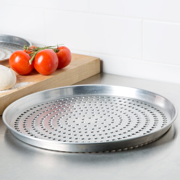 An American Metalcraft Super Perforated Heavy Weight Aluminum pizza pan with tomatoes and cheese on it.