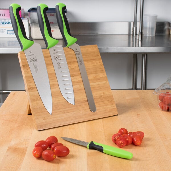 A Mercer Culinary Millennia Colors knife set on a bamboo magnetic board with green and black handles.