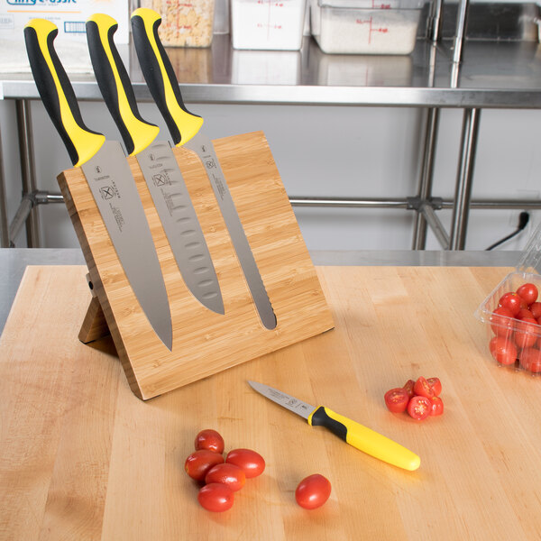 A Mercer Culinary Millennia Colors® knife set with yellow handles on a bamboo magnetic board.
