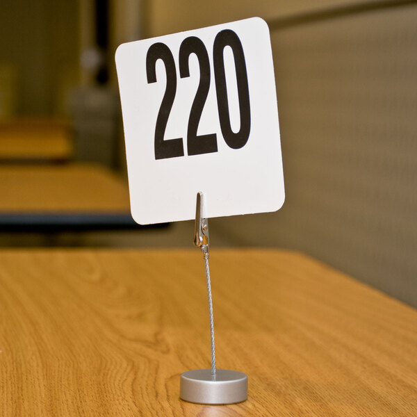 An American Metalcraft aluminum alligator clip card holder with a number sign on a table.