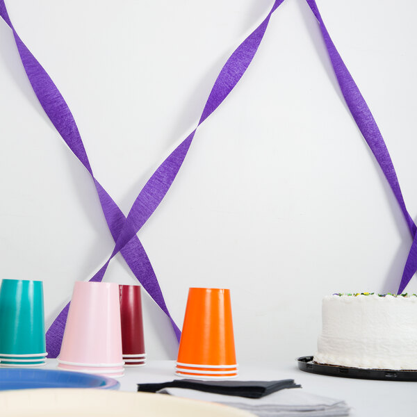 A table with a cake and purple streamer paper on it.