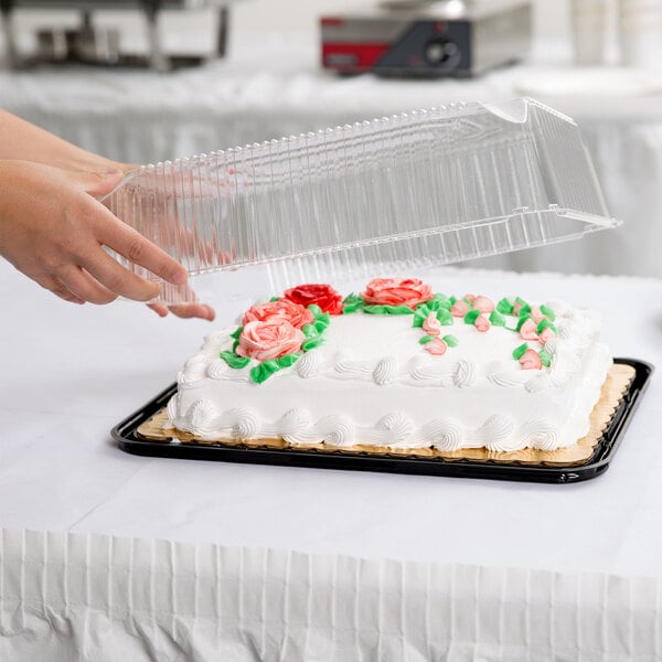 A hand using a D&W Fine Pack plastic container to cover a frosted sheet cake.