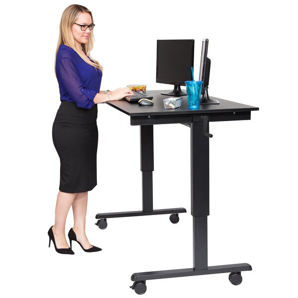 A woman standing at a black Luxor stand up desk with a computer monitor.