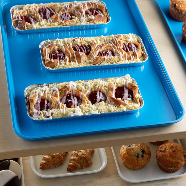 A blue Cambro market tray of pastries and muffins on a bakery display shelf.
