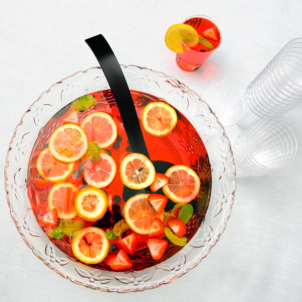 A clear plastic punch bowl filled with fruit and a glass of red punch with a slice of orange.