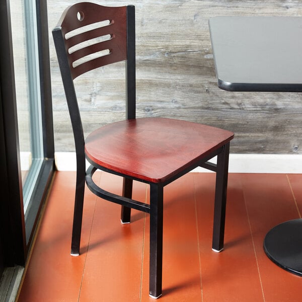 A Lancaster Table & Seating black bistro chair with a mahogany wood seat and back at a table in a restaurant.