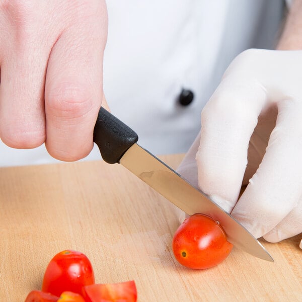 A person in white gloves using a Victorinox spear point paring knife to cut a tomato.