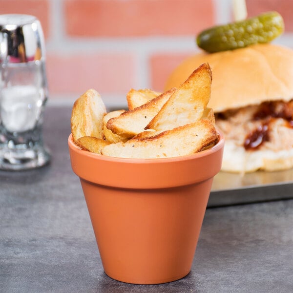 An American Metalcraft terra cotta melamine pot filled with potato wedges on a table with a burger.