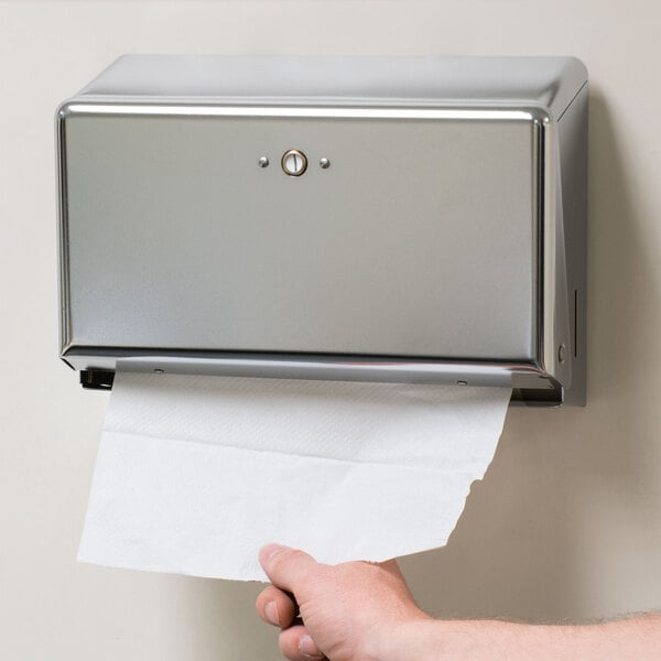 A person's arm pulling a paper towel out of a silver San Jamar paper towel dispenser.