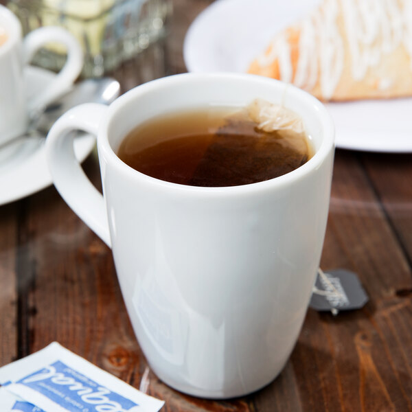 A close up of a 10 Strawberry Street white porcelain barrel mug filled with tea and a tea bag.