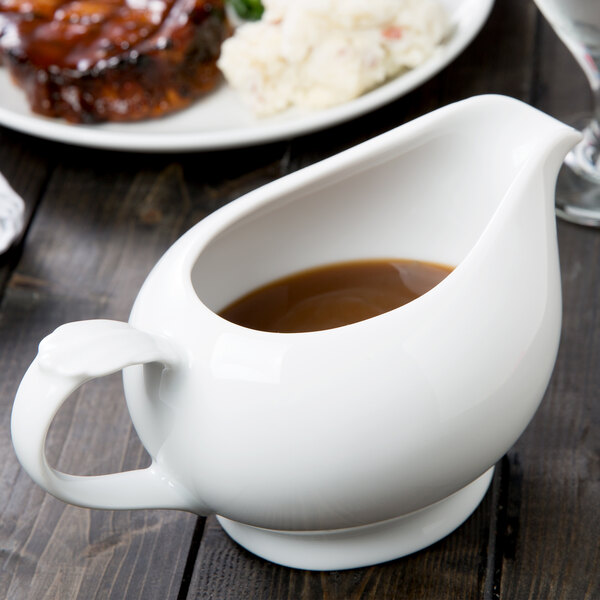 A white 10 Strawberry Street porcelain gravy boat on a table with brown gravy in it.