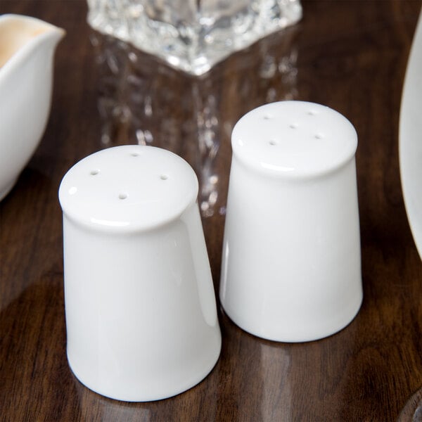 Two white porcelain salt and pepper shakers on a table.