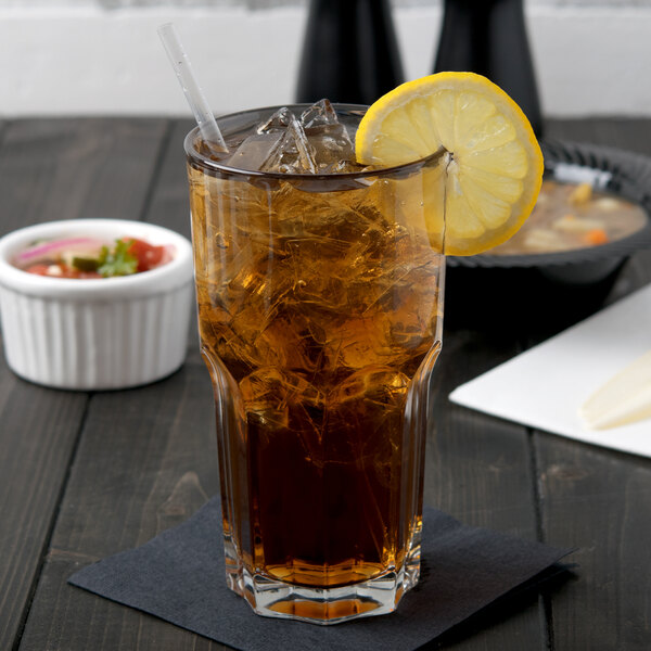 An Arcoroc stackable beverage glass of iced tea with a lemon slice on a table.