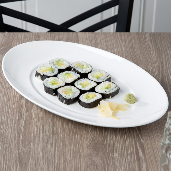 A white 10 Strawberry Street oval porcelain platter with sushi rolls on a wood table.