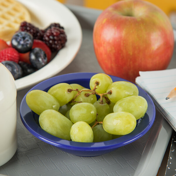 A tray with a bowl of grapes and a Carlisle dark blue polycarbonate fruit dish filled with fruit.