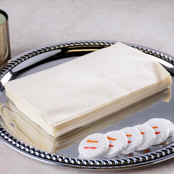 A stack of Hoffmaster ecru linen-like guest towels on a tray next to a plate of cookies.
