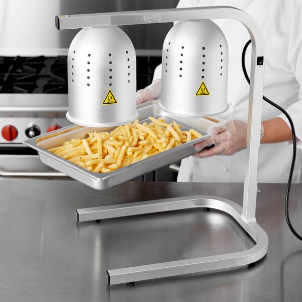 A person using an Avantco countertop heat lamp to warm a tray of french fries.