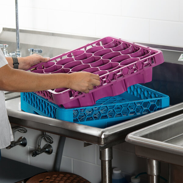 A person holding a purple and blue Carlisle OptiClean long glass rack extender over a sink full of dishes.