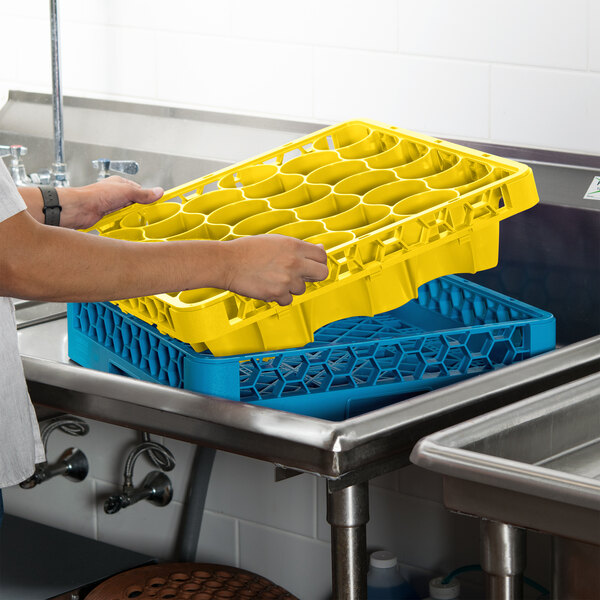 A person holding a yellow Carlisle glass rack extender over a blue dishwasher.