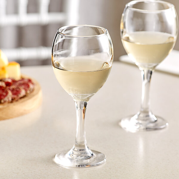 Two Acopa Bouquet wine glasses filled with white wine on a counter.