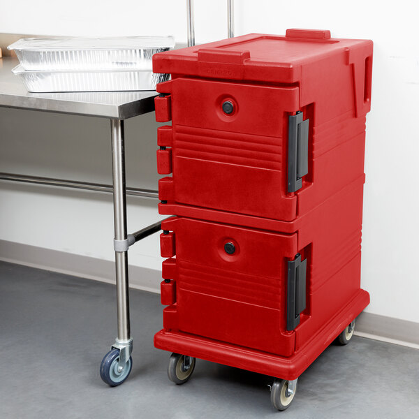 A red plastic Cambro Ultra Camcart food pan carrier on wheels with black handles.
