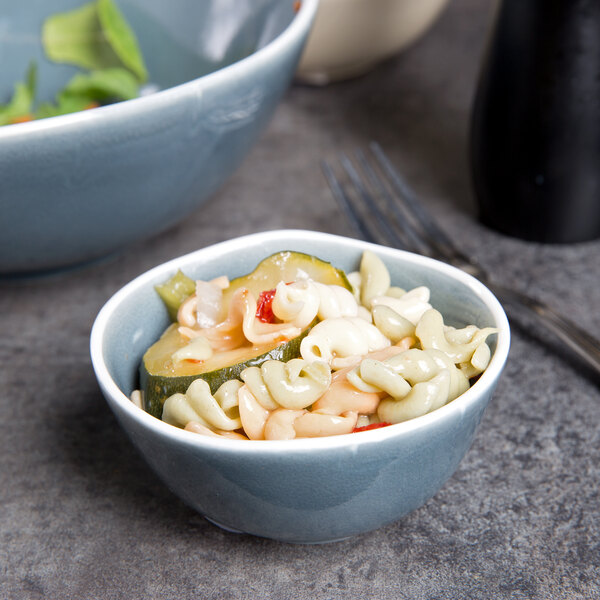A bowl of pasta with vegetables in a blue and white Arcoroc bowl.