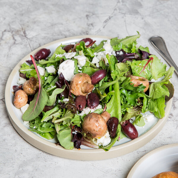 A close-up of a salad with mushrooms, olives, and greens on a Chef & Sommelier Geode salad plate.