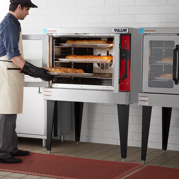 A man in an apron using a Vulcan electric convection oven to bake bread.