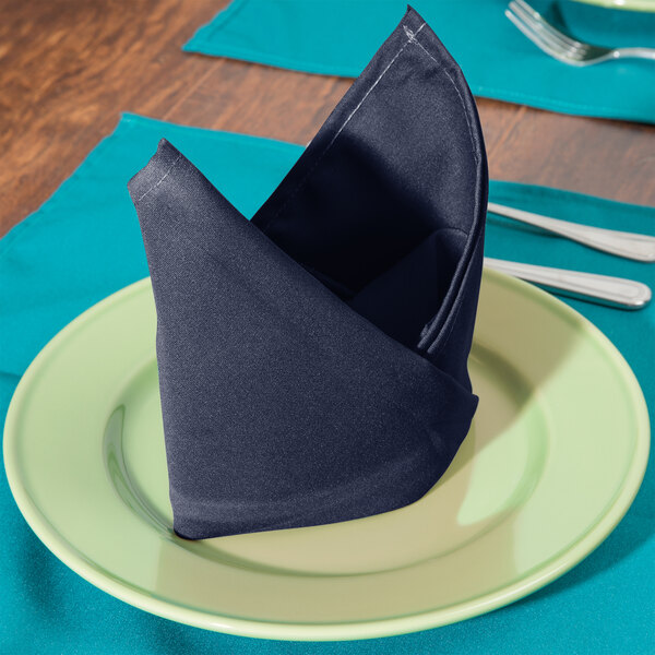 A plate with a folded Intedge navy blue cloth napkin on it.