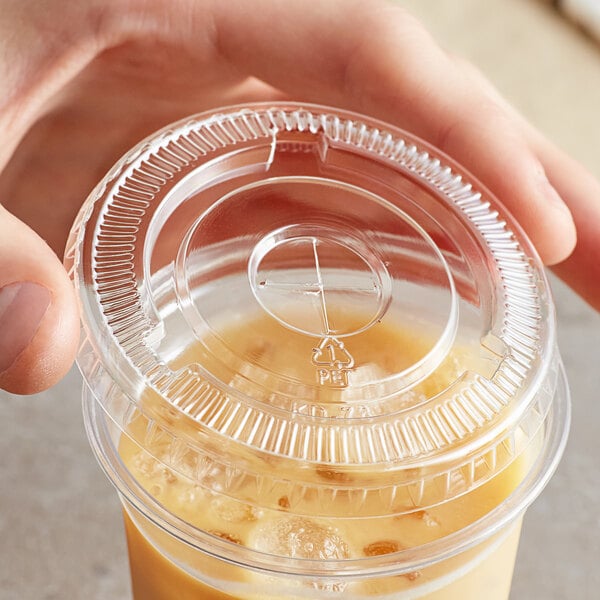 A hand holding a plastic cup with a clear plastic lid with a straw slot and a drink in it.