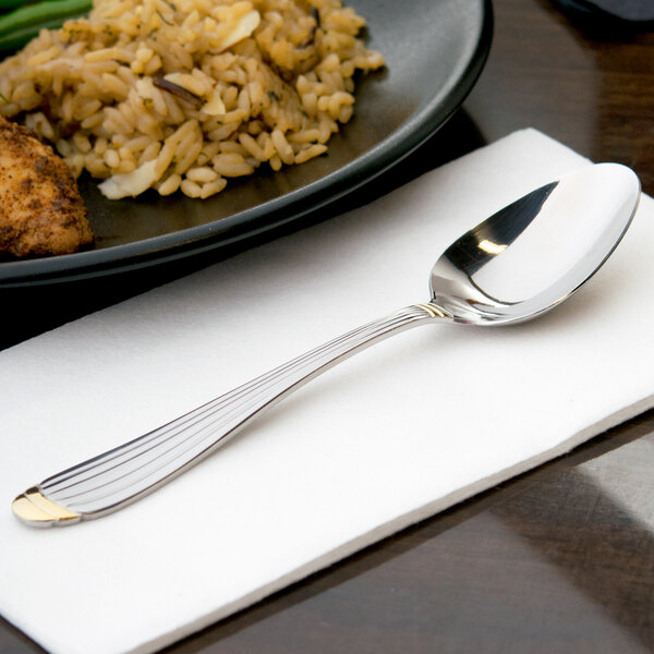 A 10 Strawberry Street Parisian gold stainless steel teaspoon on a napkin next to a plate of food.