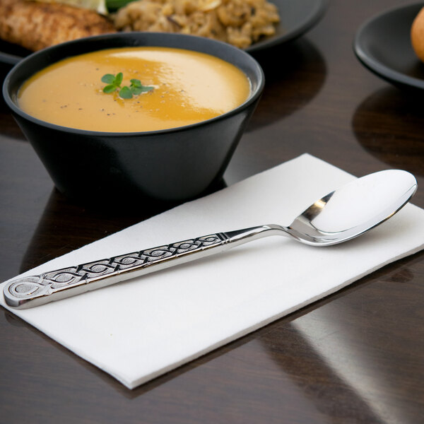 A bowl of soup with a 10 Strawberry Street Dubai stainless steel dinner spoon on a napkin.