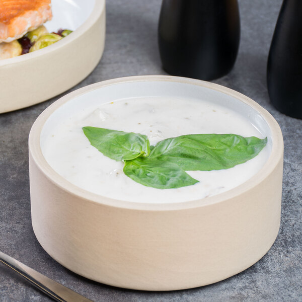 A Chef & Sommelier stoneware bowl filled with soup and basil leaves on a white background.